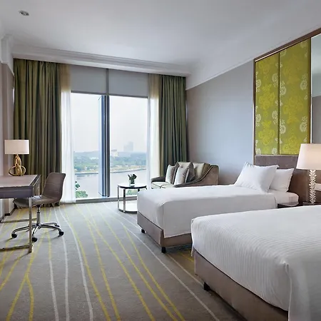 Dorsett Putrajaya Hotel Ruang foto The photo shows a modern hotel room featuring two single beds with white linens. There is a stylish desk and chair positioned beside a large window that allows natural light to fill the space. The window is adorned with long, light green curtains. A 